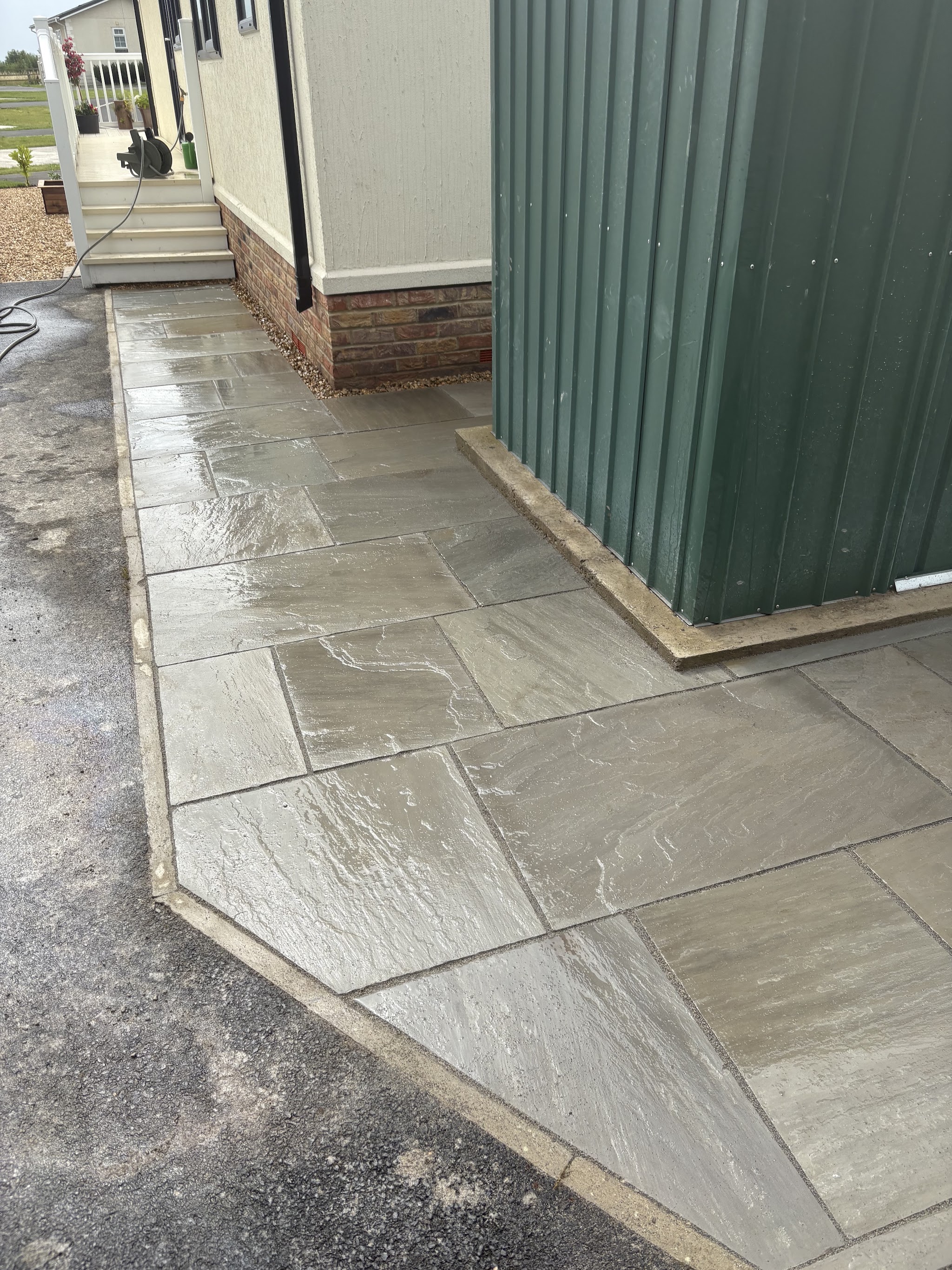 Newly laid grey slab path running alongside a green garden shed, freshly washed down