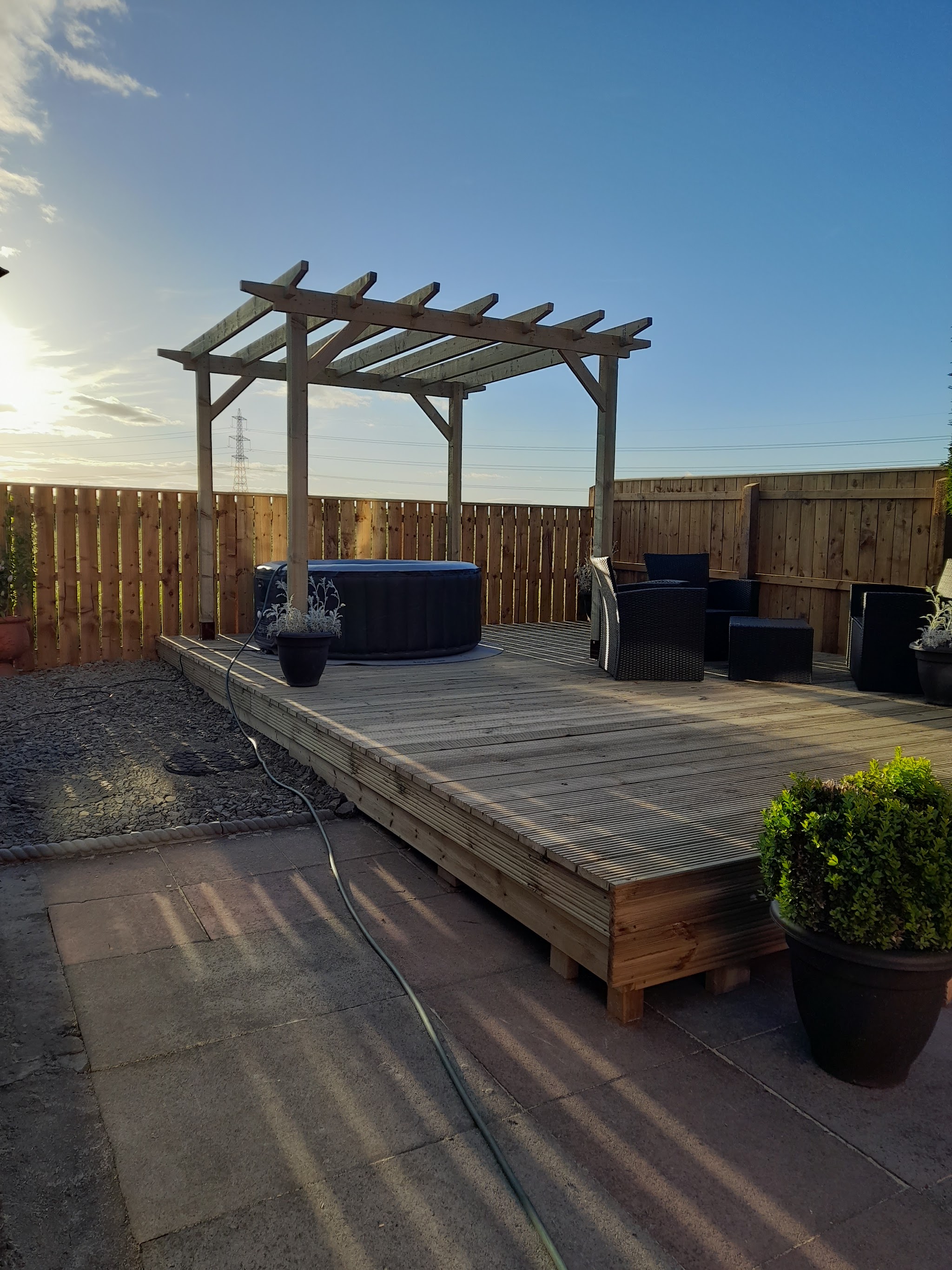Timber pergola over a new deck with a hot tub and garden furniture at sunset