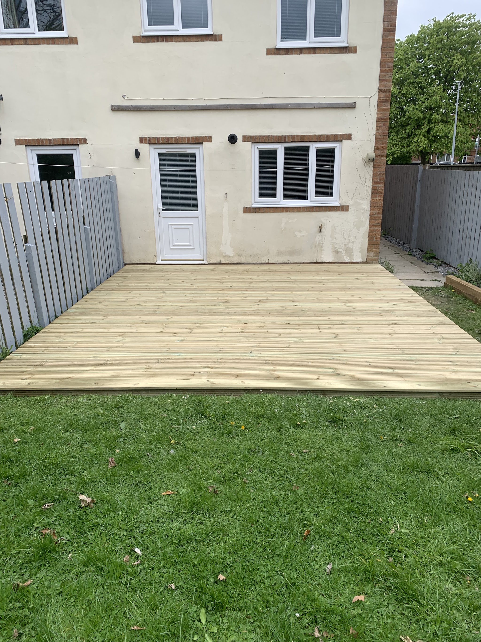 New timber deck across the back of a house with grey fencing either side and a lawn in front