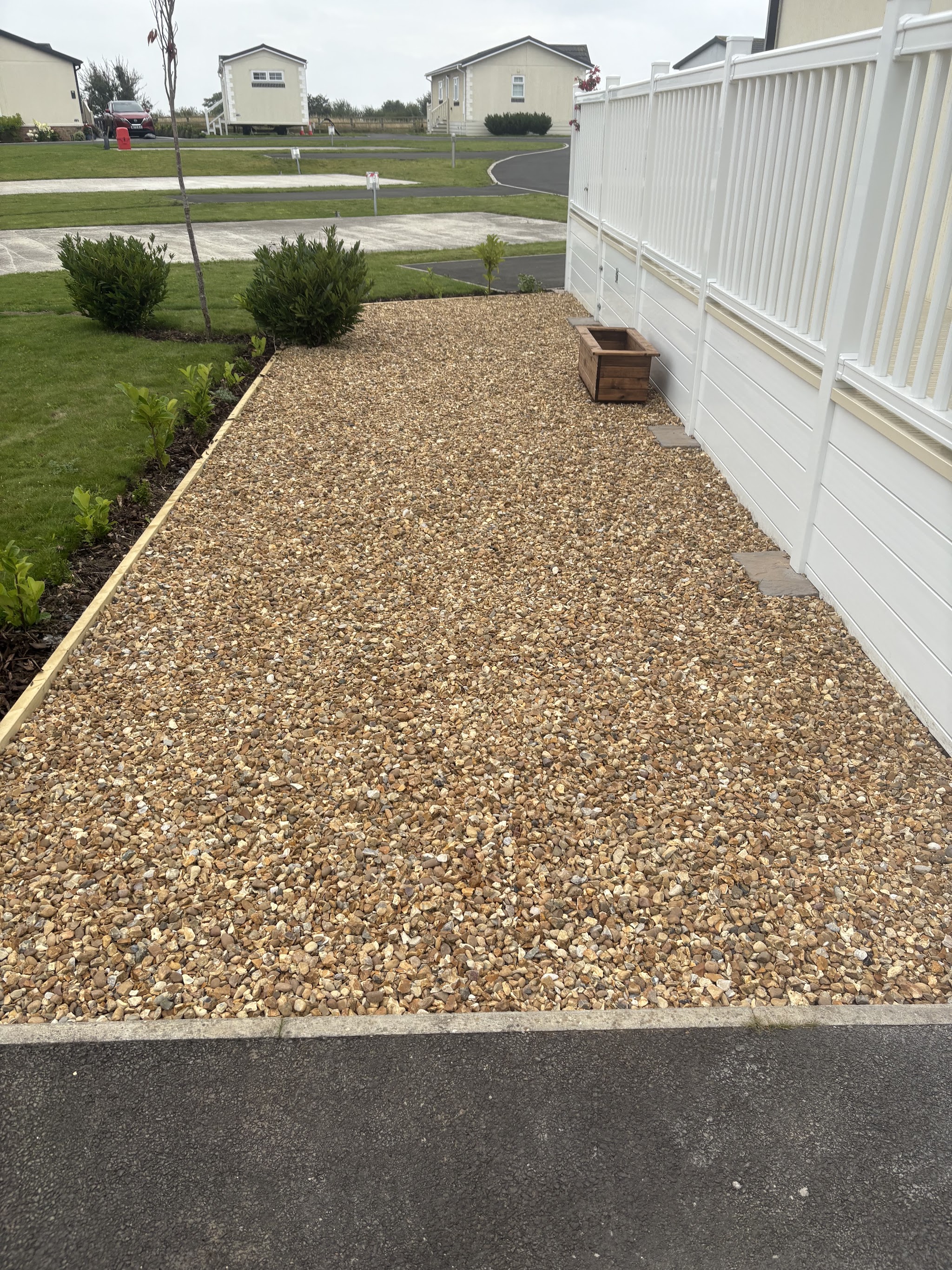 Long gravel path with timber edging beside a white fence and a strip of lawn and shrubs