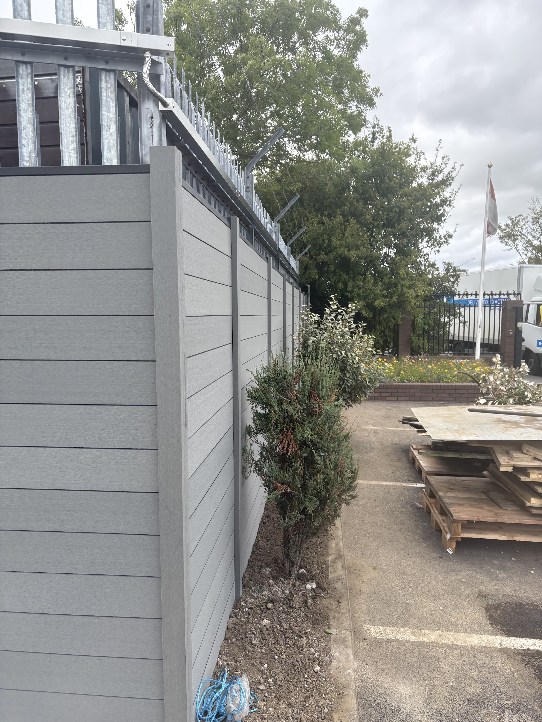 Tall grey composite fence fitted along a boundary next to a car park