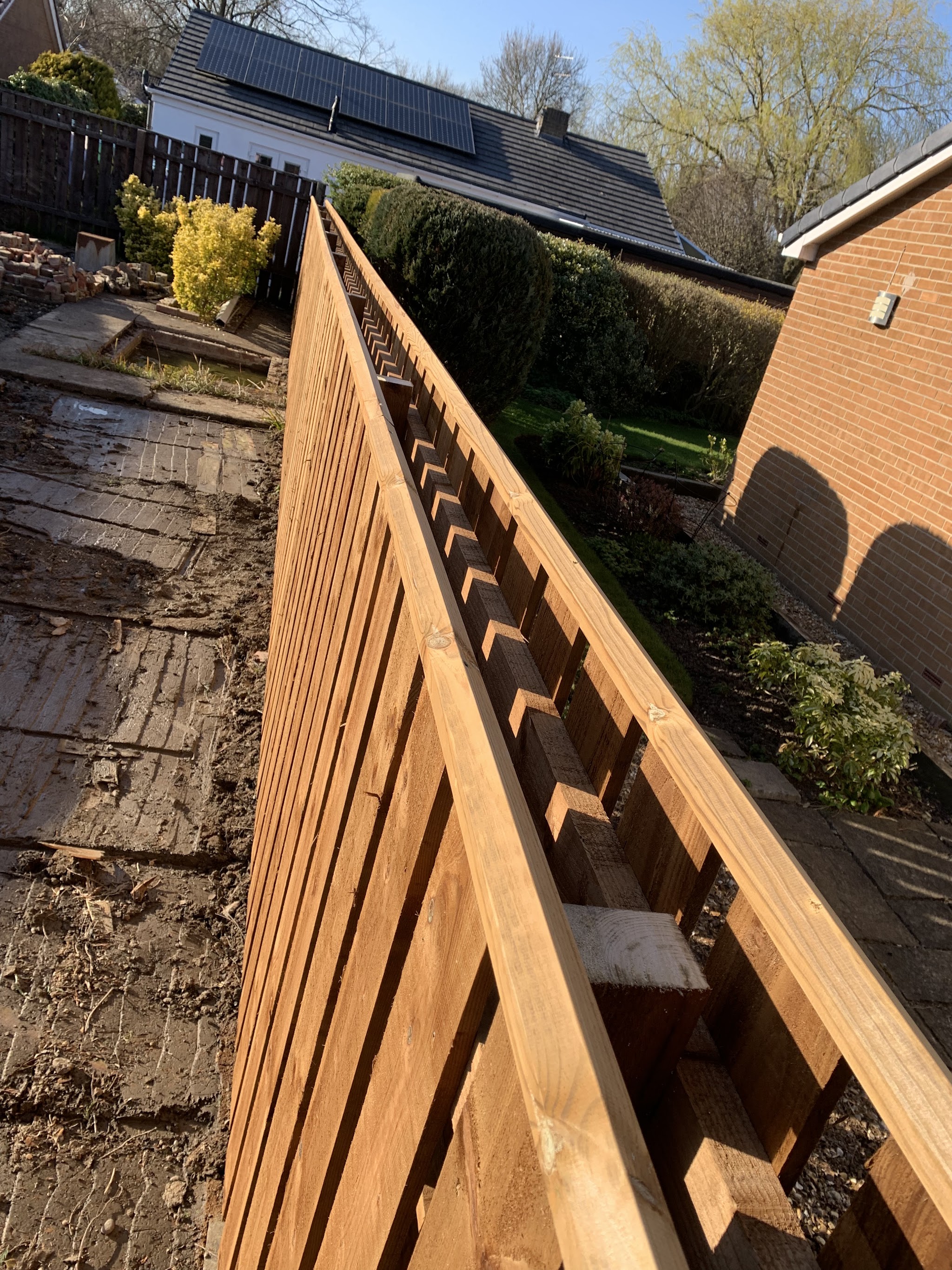Freshly fitted featheredge fence running down a sloping garden beside a brick house